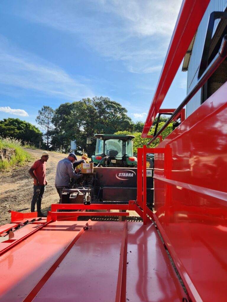 Máquina agrícola sendo puxada por um trator enquanto homens trabalham nela