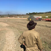 Homem de chapéu observando trator trabalhando no campo